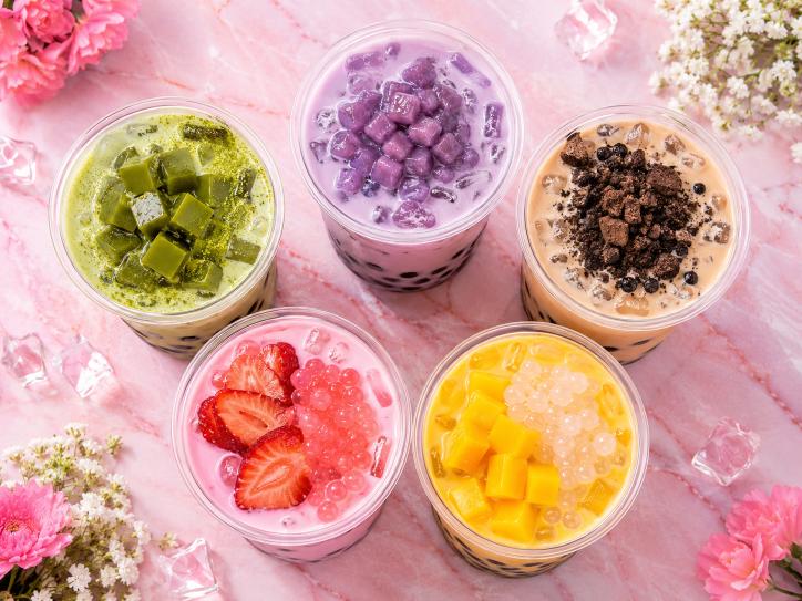 Five colourful bubble tea drinks with different toppings on pink marble