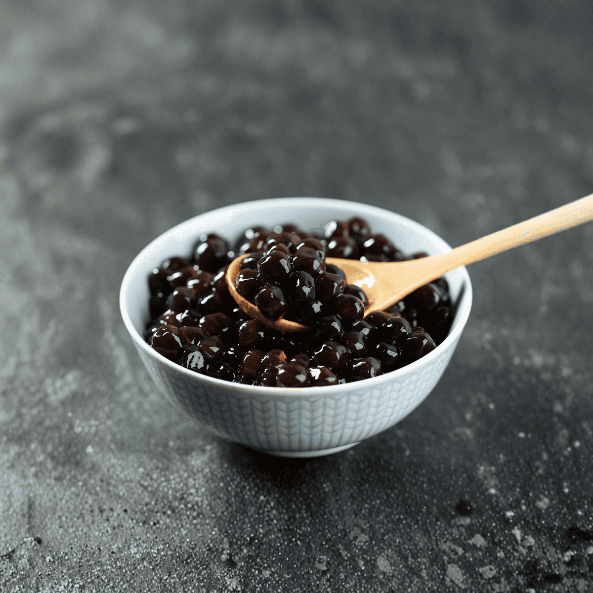 Close-up of transparent popping boba pearls in pink, orange, and green, demonstrating gel-like alginate skin encasing liquid