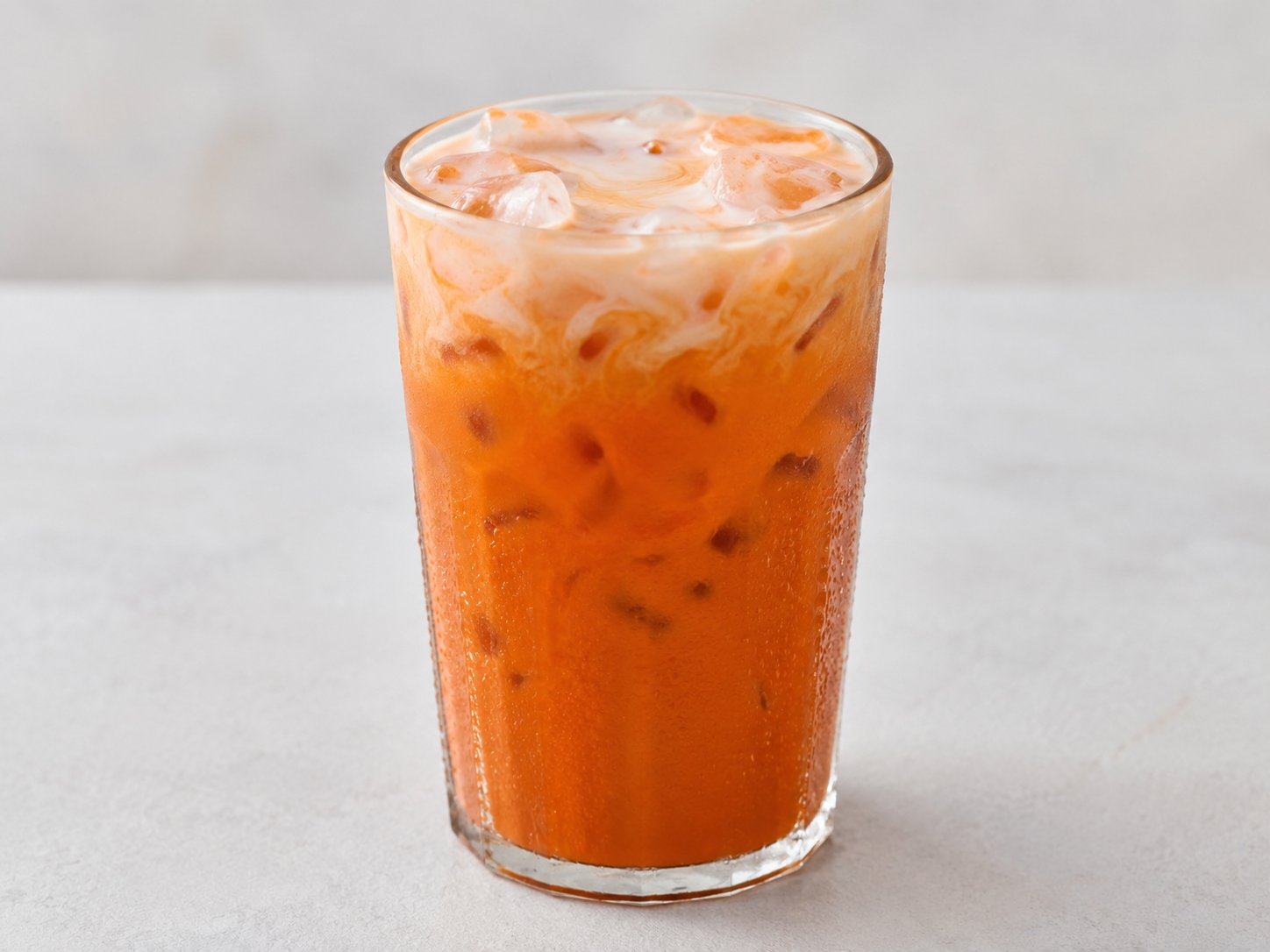Iced orange Thai milk tea in a glass cup with black tapioca boba pearls and evaporated milk swirl